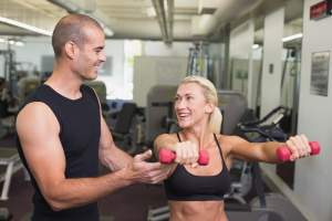 Smiling male trainer assisting woman with dumbbell in the gym